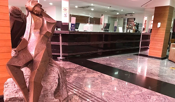 Escultura moderna em hotel, com design geométrico em ambiente elegante. Ao fundo, recepção com balcão e decoração contemporânea. Ideal para arquitetura e arte.
