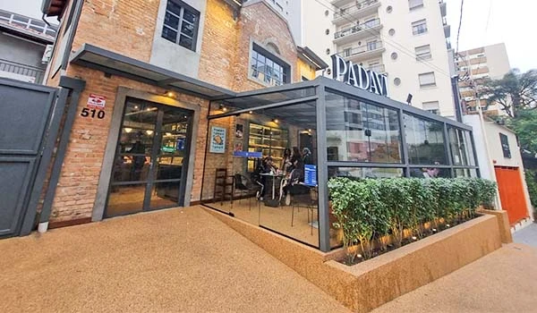 Imagem da fachada de um restaurante acolhedor com espaço interno bem iluminado, ambiente moderno e convidativo no centro de uma cidade, ideal para refeições e encontros sociais.