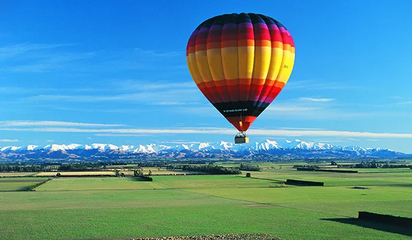 Foto em Canterbury Plains Canterbury Up and Away com balão colorido sobrevoando as bonitas paisagens verde e com montanhas nevadas na Ilha do Sul, na Lua de Mel na Nova Zelândia.