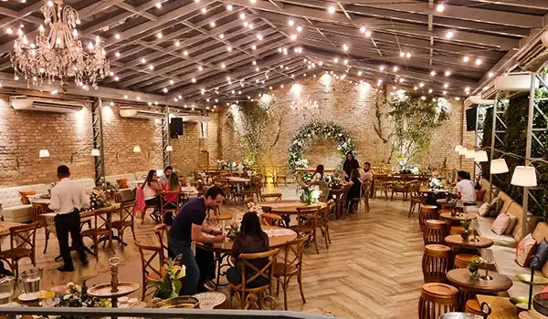 Decorado elegante de restaurante com iluminação suave, mesa de jantar, luzes pendentes, ambiente acolhedor e decoração de parede com plantas e flores. Mini Wedding em São Paulo.