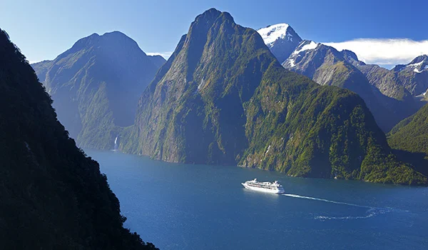 Foto de um dos fiordes da Nova Zelândia, na Ilha do Sul visto de alto com montanhas e navio navegando.