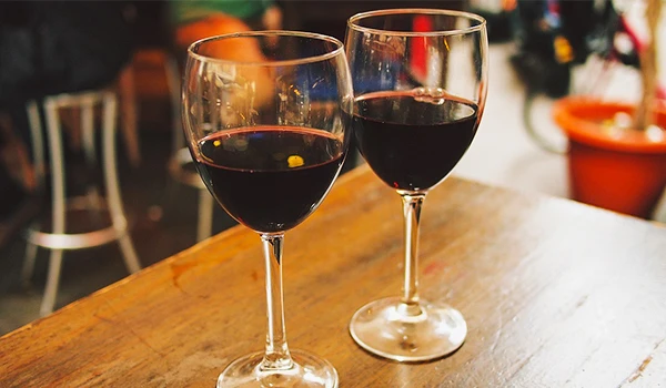 Dois copos de vinho tinto em uma mesa de madeira, com um ambiente aconchegante ao fundo, perfeito para momentos de degustação e relaxamento.