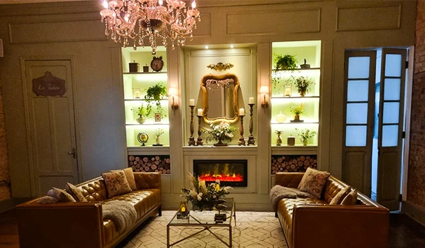 Sala de estar elegante decorada com sofás de couro, uma lareira moderna com efeito de fogo, prateleiras com plantas e objetos decorativos, iluminação suave e um lustre de cristal, um ambiente de um Mini Wedding em São Paulo.