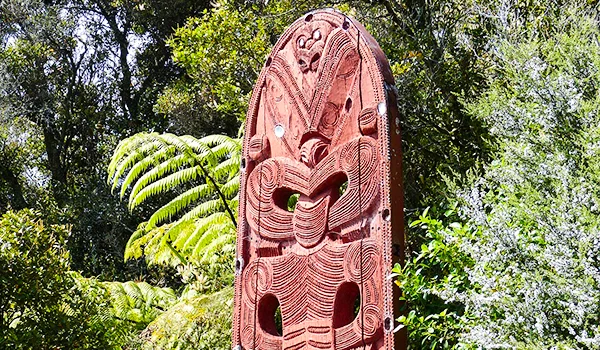 Foto de uma tábua esculpida com elementos da Cultura Maori em meio a uma floresta na Nova Zelândia
