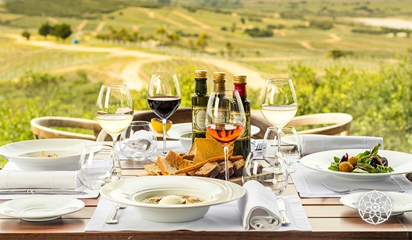 Mesa posta ao ar livre com vinho, comida e ambiente de campo, ideal para jantar romântico ou celebrações especiais.