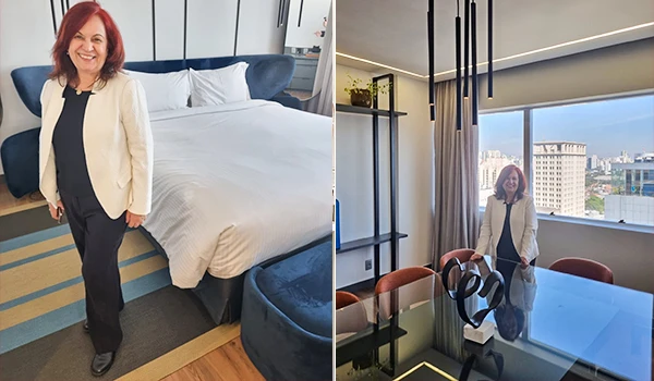 Deusa Rodrigues na suíte presidencial do Hotel Pullman em São Paulo com decoração elegante, quarto confortável e vista panorâmica de cidade ao fundo.