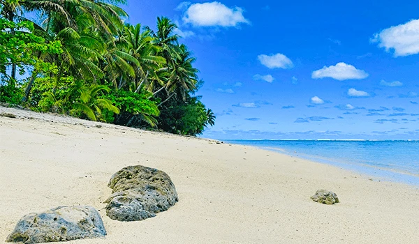 Foto de uma praia deserta com areia branca, coqueiros e céu azul naViagem para as Ilhas Cook.