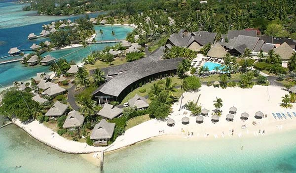 Imagem aérea de um resort de luxo à beira-mar com cabanas, piscina e áreas verdes em um destino paradisíaco com praias de areia branca e água cristalina.