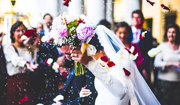 Casamento tradicional com noiva jogando buquê para as convidadas em um local ao ar livre, com convidados sorrindo e celebrando o momento.