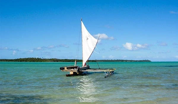Barco à vela navegando em águas cristalinas com céu azul e ilha ao fundo, perfeito para atividades de lazer e esportes aquáticos.