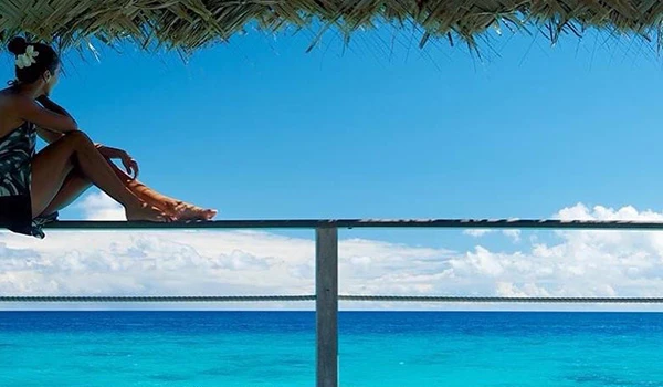 Mulher aproveitando a vista do mar sob uma cabana de praia, relaxando e curtindo o clima tropical com céu azul e águas cristalinas na Polinésia Francesa.