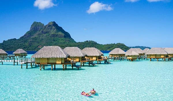 Lindo resort de águas cristalinas e bangalôs sobre a água, com uma montanha ao fundo em uma ilha paradisíaca, ideal para férias e relaxamento. Polinésia Francesa.