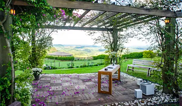Imagem de um espaço ao ar livre com uma vista de natureza, incluindo uma área de estar com cadeiras, mesa de centro, iluminação suave e um jardim florido ao redor, perfeito para momentos de relaxamento ao ar livre.
