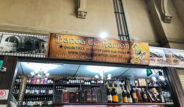 Banca do Ramon, uma loja de bebidas localizada no Mercado Municipal Paulistano, com destaque para uma variedade de vinhos e destilados em exibição.