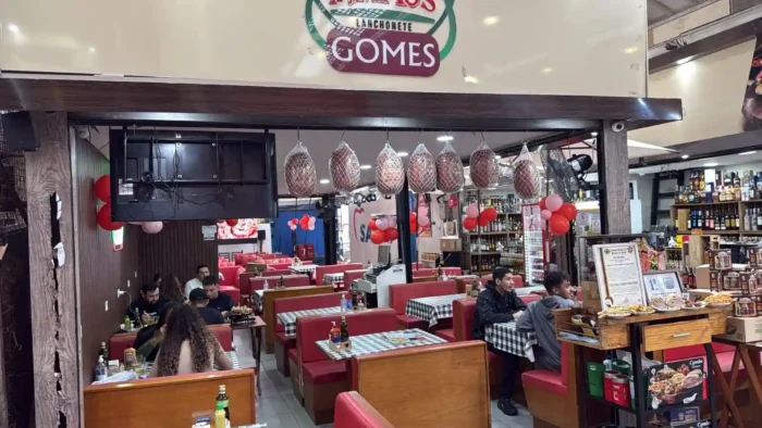 Ambiente de uma lanchonete com decoração temática, mesas com toalhas quadriculadas, na Adega Irmãos Gomes no Mercadão de São Paulo.