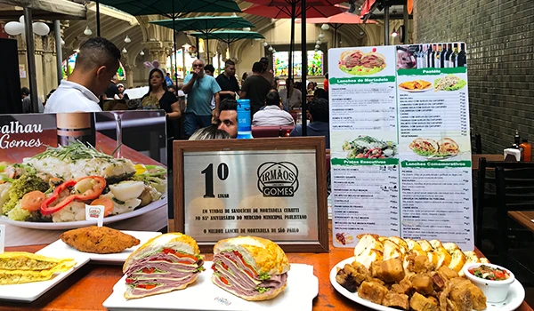 Ambiente sobre onde comer no Mercadão de São Paulo, com comidas com pratos tradicionais, sanduíches, uma verdadeira feira gastgronômica.