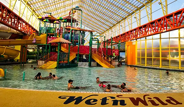 Imagem do parque aquático Wet'n Wild, apresentando toboáguas coloridos, áreas de lazer interna e visitantes se divertindo na piscina.