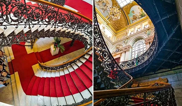Escadaria interna ornamentada do Palácio da Liberdade, com degraus revestidos de vermelho, corrimãos de madeira e elaborados detalhes em ferro forjado. A segunda imagem mostra a escadaria em perspectiva, destacando a arquitetura neoclássica, vitrais, pinturas decorativas e elementos dourados. Visita ao Palácio da Liberdade.