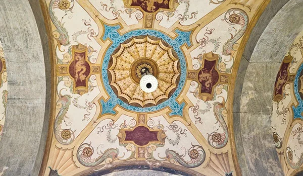 Teto ricamente ornamentado do Palácio da Liberdade, com uma grande rosácea central dourada, cercada por arabescos, motivos florais e detalhes em azul, vermelho e creme. Arcos de pedra emolduram a composição nas laterais. Visita ao Palácio da Liberdade.