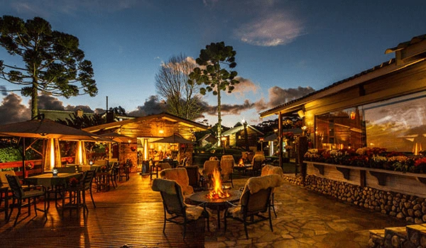 Vista de um bonito restaurante com mesas ao ar livre, e cenário do fim de tarde em Campos do Jordão, dicas sobre onde comer na Serra da Mantiqueira.