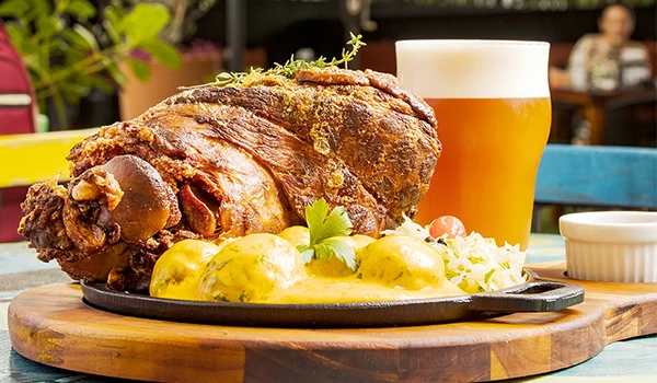 Prato saboroso com joelho de porco crocante, acompanhado de batatas e chopp gelado em ambiente descontraído, ideal para um jantar saboroso.