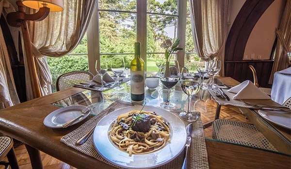 Foto de uma mesa posta com prato de massa e carne, e taças com vinho branco, no restaurante Toribinha no Hotel Toriba, uma das dicas sobre onde comer na Serra da Mantiqueira.