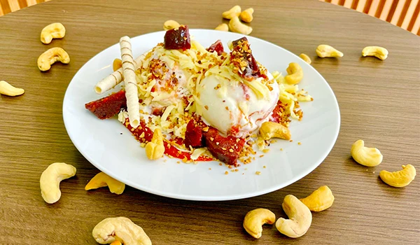 Sobremesa deliciosa com sorvete, pedaços de chocolate e castanhas de caju, servida em um prato branco sobre mesa de madeira.