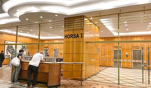 Recepção do edifício Horsa I, com acabamento em madeira e iluminação moderna, mostrando pessoas interagindo no local.