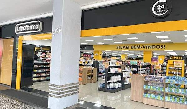 Foto da fachada da Ultrapar, uma farmácia aberta 24 horas, decorada em amarelo e preto, com prateleiras repletas de produtos variados.