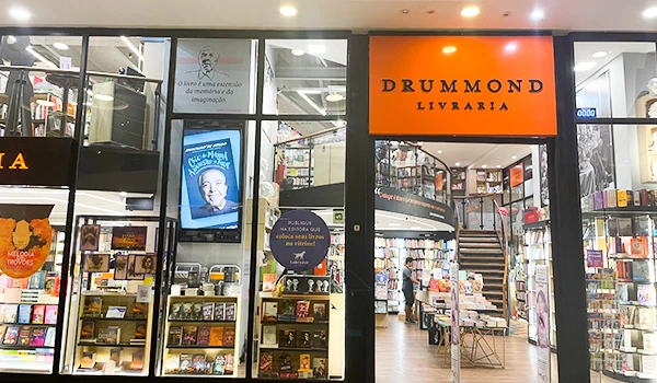 Imagem da fachada da Livraria Drummond, mostrando a entrada e as prateleiras de livros, ideal para amantes da leitura e cultura.