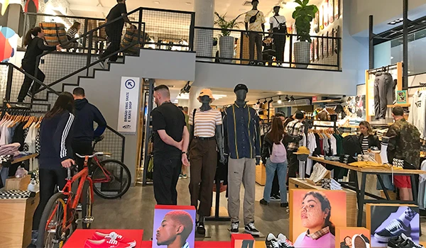 Loja de roupas moderna com várias pessoas, manequins e produtos em exibição, representando um ambiente jovem e urbano. A imagem destaca a moda atual e as tendências de vestuário.