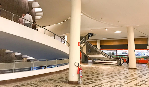 Imagem da arquitetura de um shopping, destacando escadas rolantes e um elegante design de interior com piso em padrão geométrico. Dicas do Conjunto Nacional em São Paulo.