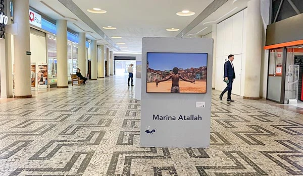 Imagem de uma exposição de arte com uma obra de Marina Atallah em destaque em um ambiente de shopping. A obra retrata um personagem que interage com a paisagem. Dicas do Conjunto Nacional em São Paulo.