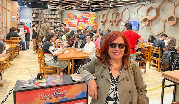 Deusa Rodrigues em um ambiente aconchegante com decoração moderna e estantes de livros ao fundo.