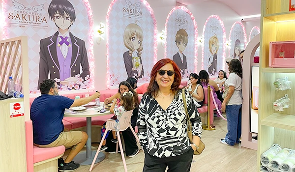 Deusa Rodrigues desfrutando do Café Cardcaptor Sakura, um espaço temático inspirado em anime com decoração delicada, imagens de personagens famosos e ambiente acolhedor.