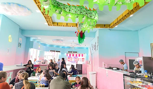 Foto da Doceria Kureiji Candy com clientes em mesas, com balcão de doces na lateral e no teto um enorme dragão na cor verde.