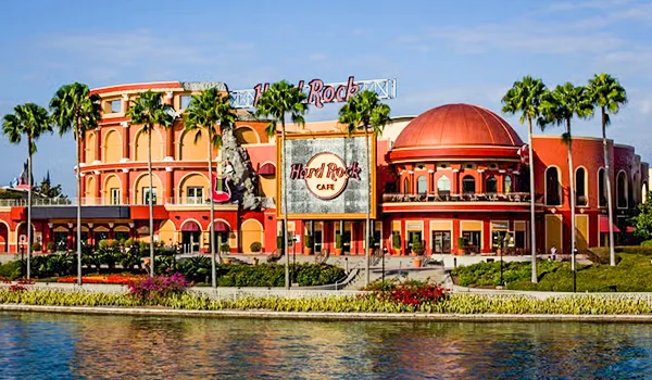 Foto do Hard Rock Café prédio em cores laranja e vermelho, tendo jardim e coqueiros a frente.