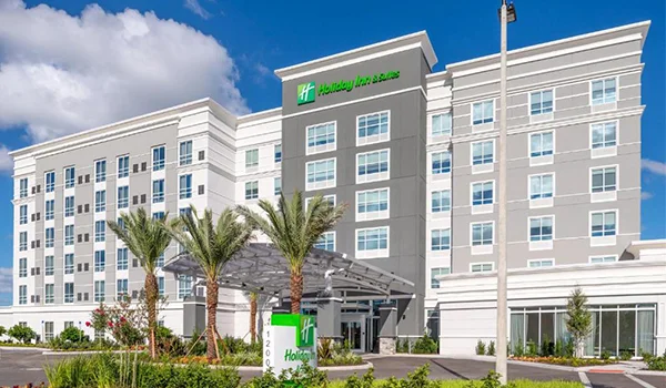 Foto do prédio moderno e clássico do Holiday Inn Suites com coqueiros a frente da fachada.