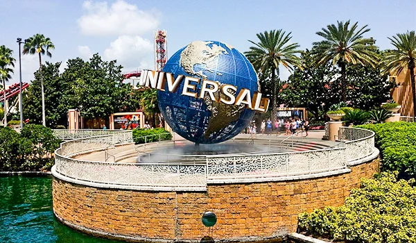Foto do globo do mundo com o logo Universal na entrada do parque em meio a palmeiras e jardins.
