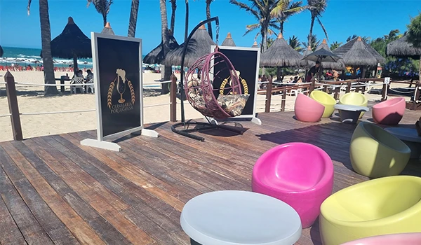 Imagem de uma área de praia com cadeiras coloridas, cabanas de palha e cabanas na areia, com o mar ao fundo e um céu azul claro, ambiente de lazer e relaxamento. Hospedagem no Vila Galé Fortaleza.