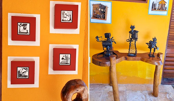 Decoração de parede com quadros e pequenas esculturas de personagens robóticos em uma sala com parede amarela, criando um ambiente artístico e moderno.