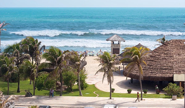 Praia paradisíaca com ondas do mar, coqueiros, áreas verdes e estrutura de lazer, ideal para descanso e lazer na natureza.