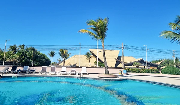 Piscina ao ar livre em um resort com palmeiras e céu azul claro, ideal para lazer e descanso na praia ou piscina tropical.
