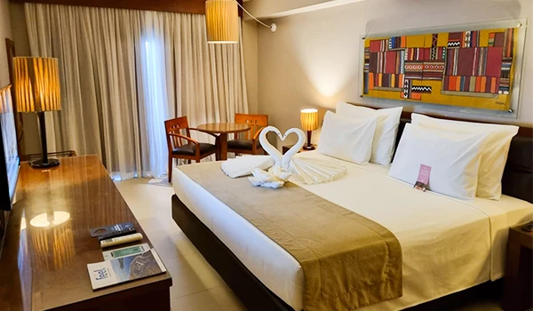 Quarto de hotel confortável e bem decorado, com cama de casal, cortinas grossas, mobília moderna e uma decoração elegante com swan de toalhas na cama.