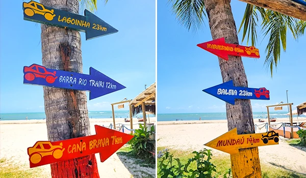 Sinalizações coloridas apontando destinos turísticos na praia, incluindo Lagoinha, Barra Rio Trairi, Canãa Brava, Mundaú, Ilha Bela e Metrôégio Gemb