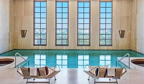 Área de piscina coberta tendo na parede grandes vidraças que mostram a cidade de São Paulo, no hotel 