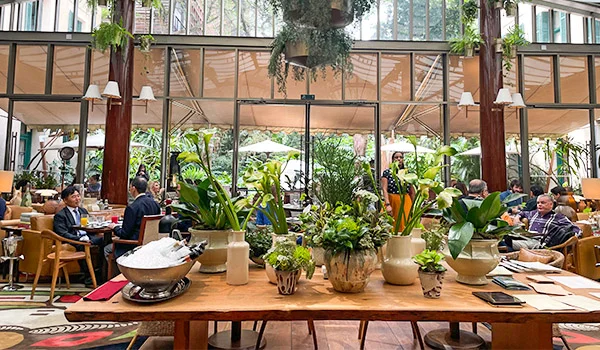 Foto do bonito restaurante do hotel Rosewood, com mesa grande com plantas, outras mesas e cadeiras com clientes e ao fundo o jardim. Hotéis de luxo em São Paulo.