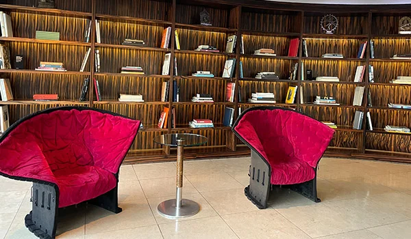 2 poltronas vermelhas tendo ao fundo uma estante com livros no lobby do Hotel Unique São Paulo.