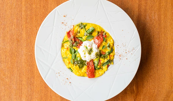 Prato de risoto com legumes coloridos, salada de queijo e tomate em prato branco, com fundo de mesa de madeira, apresentando uma refeição apetitosa