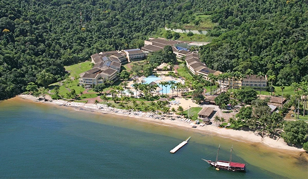 Complexo turístico localizado à beira do mar, rodeado por floresta tropical, com piscinas, hotéis e uma marina com barcos, promovendo lazer e contato com a natureza. Rota Verde Azul.
